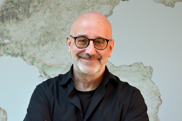 Portrait Peter Korn, black shirt, wall-filling, grayish world map in the background